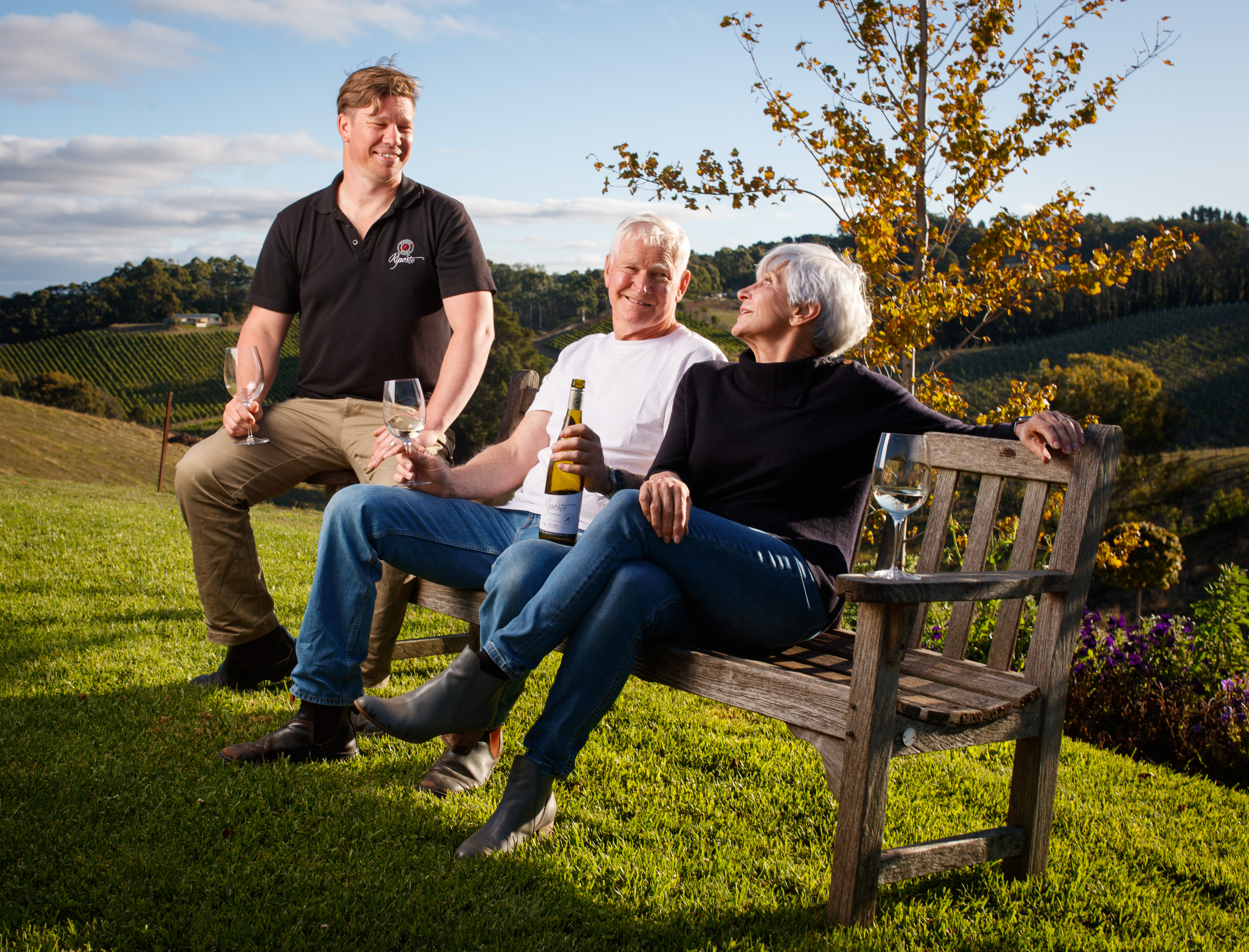 Three people sitting on a bench drinking wine